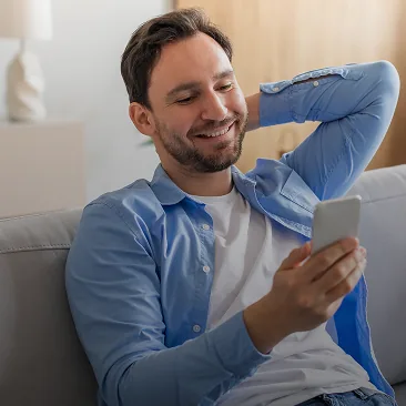 Homem sorrindo no sofá com o celular na mão